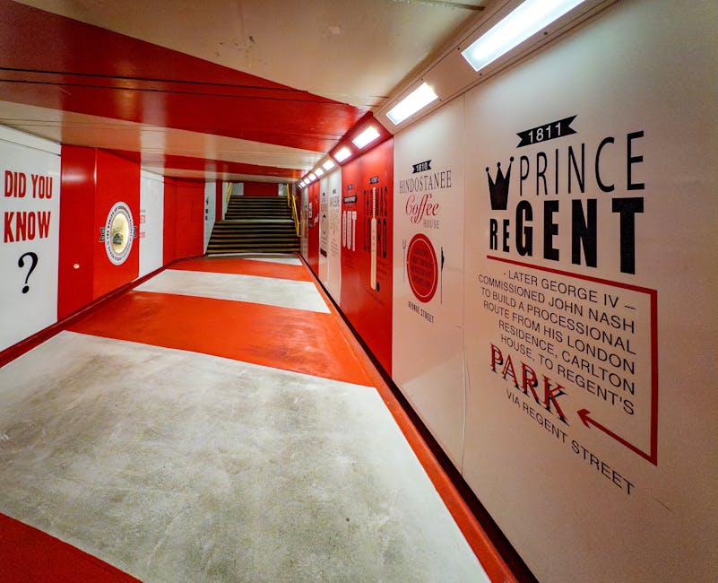 An indoor hallway with a combination of polished concrete and vibrant red and white painted surfaces, illuminated by bright overhead lighting. The concrete floor appears clean and smooth, reflecting the light, while the red and white walls feature various graphic advertisements and text, including historical references to Prince Regent and general public information. At the end of the corridor, there is a staircase with dark steps leading upward. The scene shows minimal clutter, highlighting the tidiness and maintained condition of the space, consistent with professional surface cleaning and sanitisation standards upheld by Marylebone Carpet Cleaning.