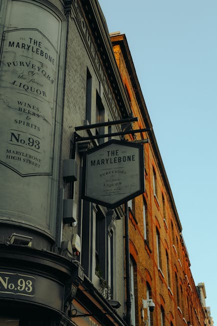 Close-up view of the exterior of The Marylebone pub in Marylebone, showing its traditional signage mounted on a building with a classic brick facade and large windows. The signage displays the pub's n